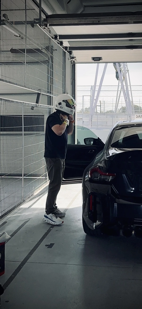 Helmeted person beside a dark car in a pit garage